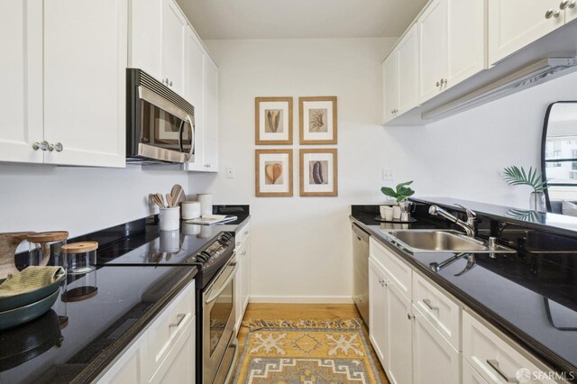 kitchen featuring stainless steel appliances, sink, white cabinetry, light wood-type flooring, and dark stone counters