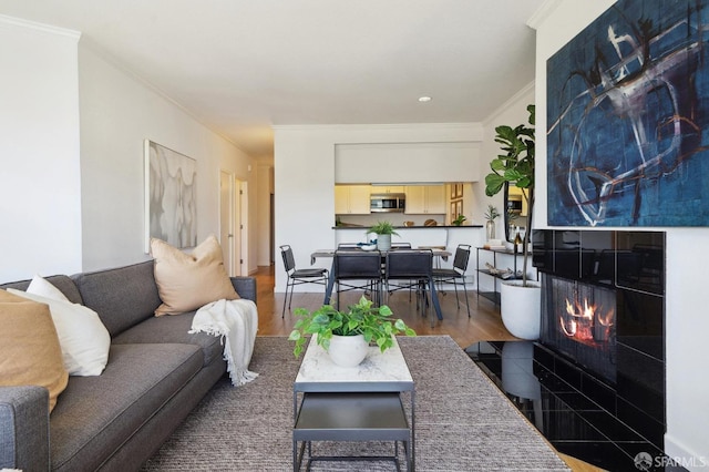 living room featuring a tiled fireplace, crown molding, and hardwood / wood-style flooring