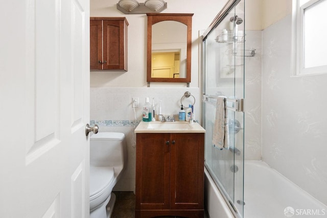 full bathroom featuring toilet, enclosed tub / shower combo, tile walls, and vanity