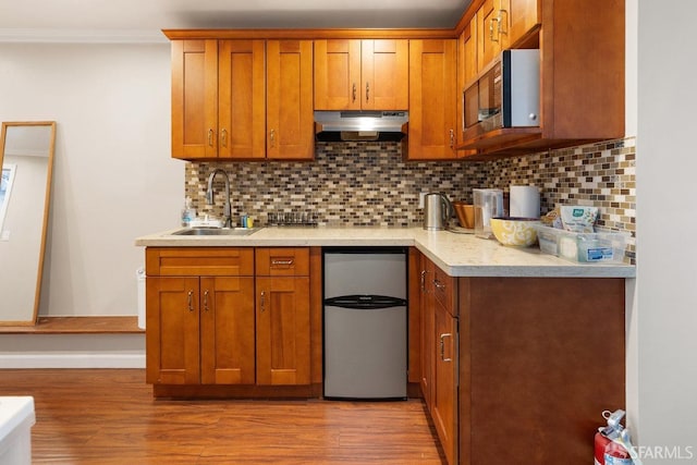 kitchen with light hardwood / wood-style floors, appliances with stainless steel finishes, backsplash, ornamental molding, and sink