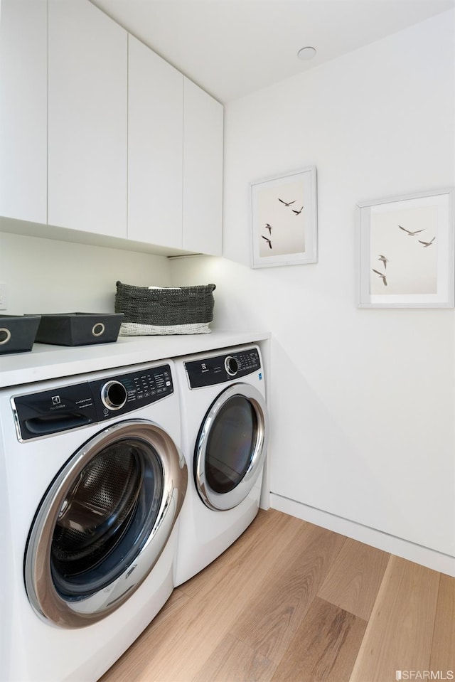 clothes washing area with cabinet space, wood finished floors, and washer and clothes dryer