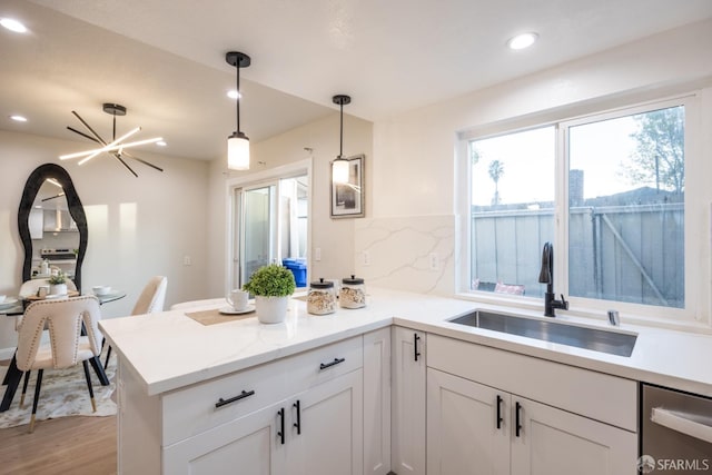 kitchen featuring decorative light fixtures, white cabinetry, sink, stainless steel dishwasher, and kitchen peninsula