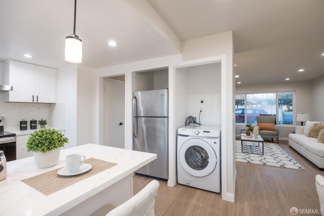 kitchen featuring washer / dryer, decorative light fixtures, light hardwood / wood-style flooring, appliances with stainless steel finishes, and white cabinets