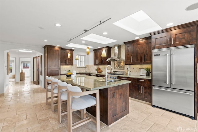 kitchen featuring a sink, stone tile floors, stainless steel built in refrigerator, and wall chimney range hood