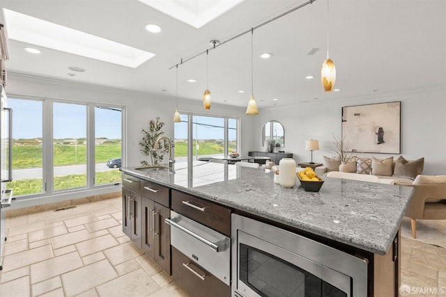 kitchen with stainless steel microwave, open floor plan, ornamental molding, a skylight, and a sink