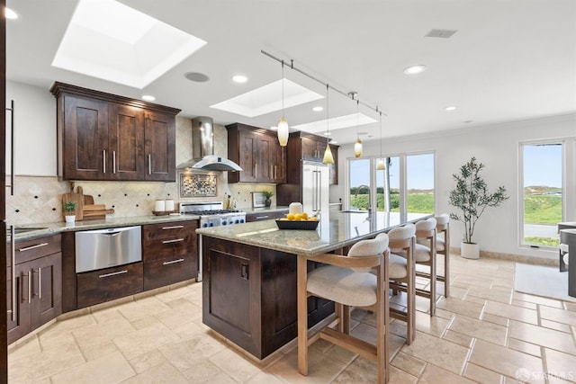 kitchen with wall chimney range hood, decorative backsplash, a skylight, a warming drawer, and a sink