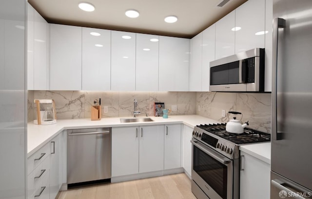 kitchen with white cabinetry, sink, stainless steel appliances, backsplash, and light wood-type flooring