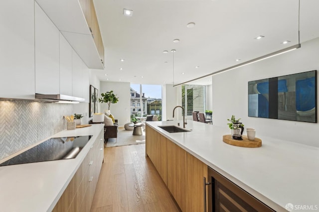 kitchen featuring sink, white cabinetry, hanging light fixtures, light hardwood / wood-style flooring, and decorative backsplash