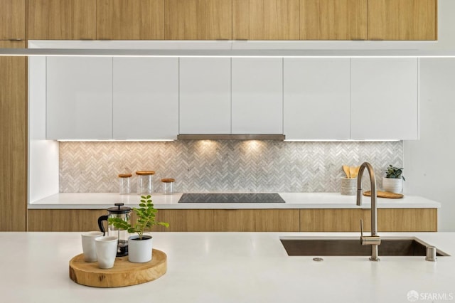 kitchen with sink, black electric stovetop, ventilation hood, white cabinets, and decorative backsplash