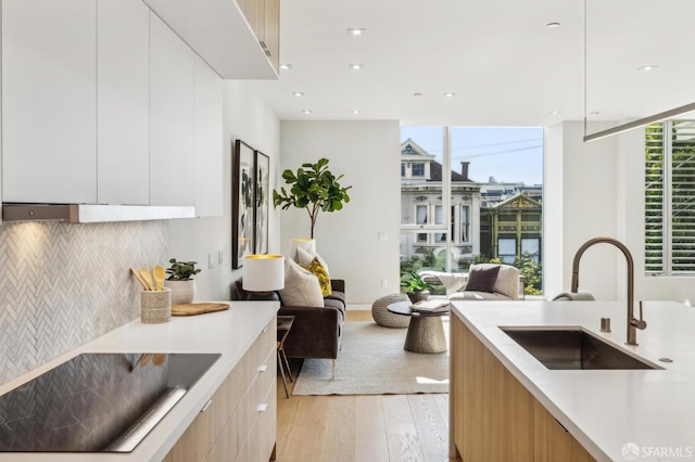 kitchen featuring sink, tasteful backsplash, expansive windows, light hardwood / wood-style floors, and white cabinets