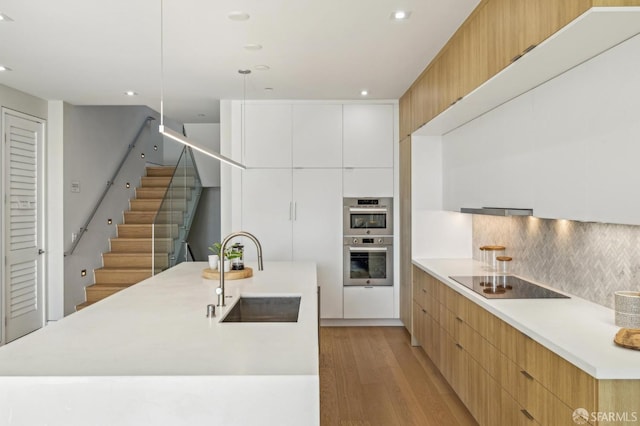 kitchen with sink, white cabinets, decorative backsplash, black electric cooktop, and light hardwood / wood-style flooring