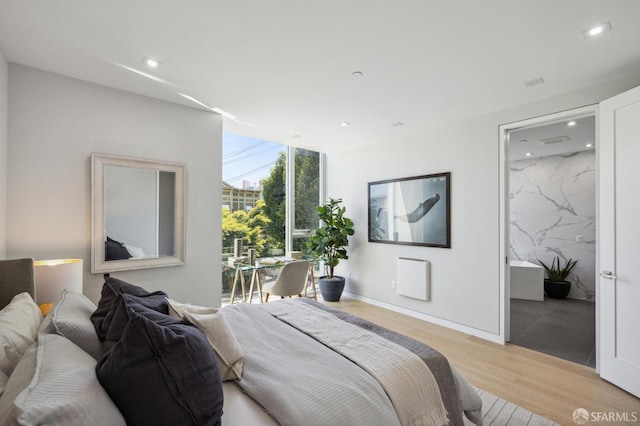 bedroom featuring connected bathroom, a wall of windows, and light wood-type flooring