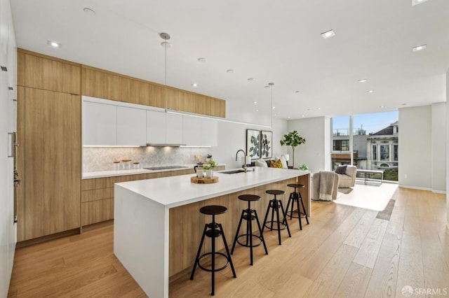 kitchen featuring white cabinetry, a spacious island, decorative backsplash, hanging light fixtures, and light hardwood / wood-style flooring