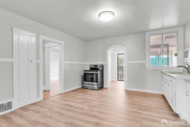 kitchen with white cabinets, a textured ceiling, stainless steel electric range oven, sink, and light hardwood / wood-style flooring