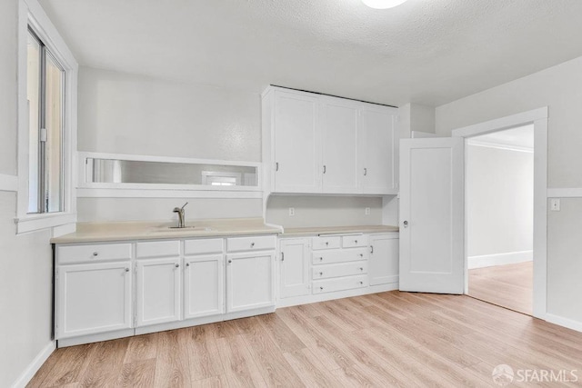 kitchen with white cabinets, light hardwood / wood-style flooring, a textured ceiling, and sink