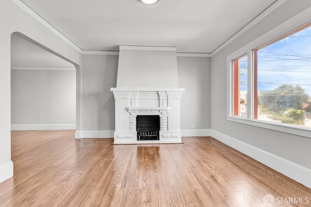 unfurnished living room featuring a brick fireplace, crown molding, and wood-type flooring