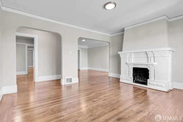 unfurnished living room featuring a brick fireplace, crown molding, and hardwood / wood-style flooring