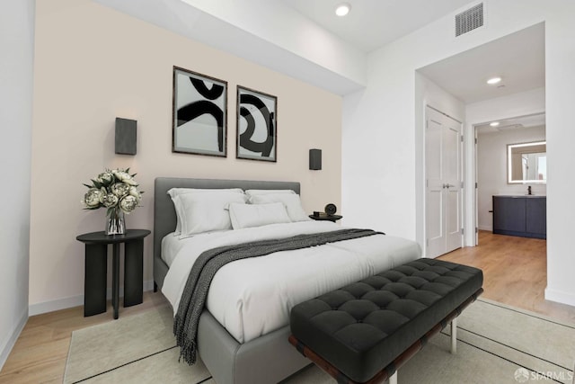 bedroom with ensuite bathroom and light hardwood / wood-style floors