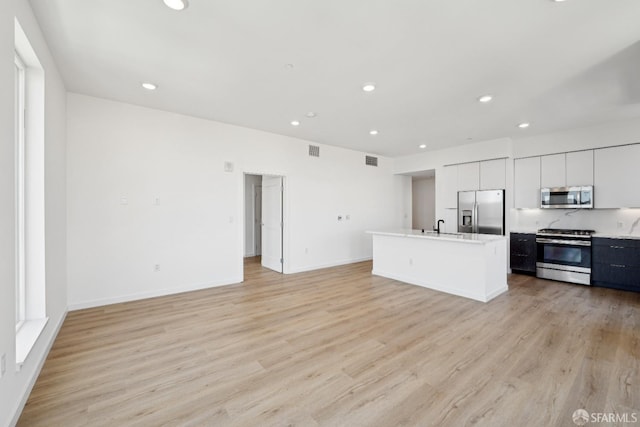 kitchen featuring appliances with stainless steel finishes, a kitchen island with sink, white cabinetry, and light hardwood / wood-style floors