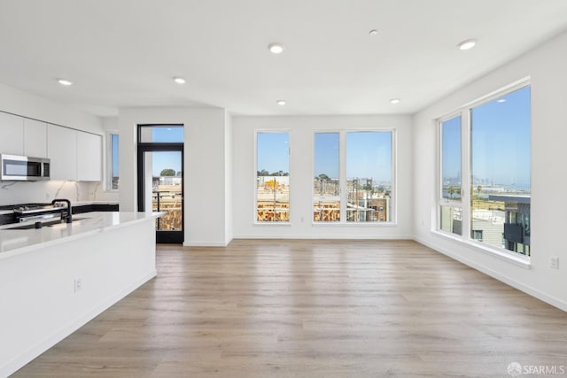 kitchen with appliances with stainless steel finishes, white cabinetry, light hardwood / wood-style floors, and a wealth of natural light