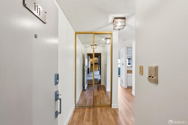 hall with light wood-type flooring and a textured ceiling