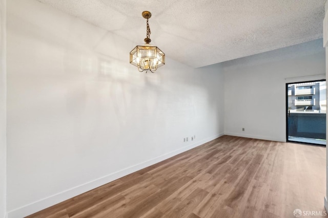 unfurnished room featuring hardwood / wood-style floors, a textured ceiling, and a chandelier