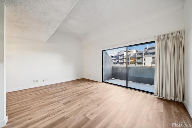 empty room with light hardwood / wood-style floors, vaulted ceiling, and a textured ceiling