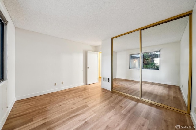 unfurnished bedroom with a textured ceiling, a closet, and light hardwood / wood-style floors