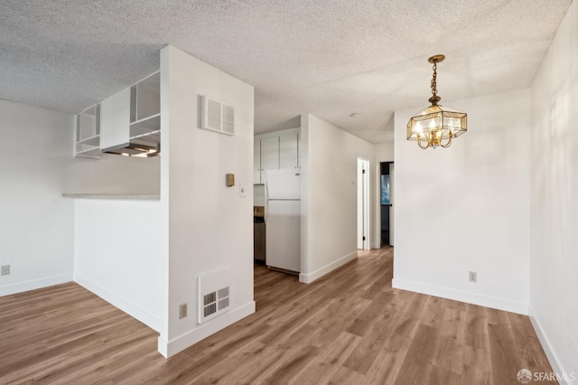 unfurnished dining area with a textured ceiling, a notable chandelier, and hardwood / wood-style floors