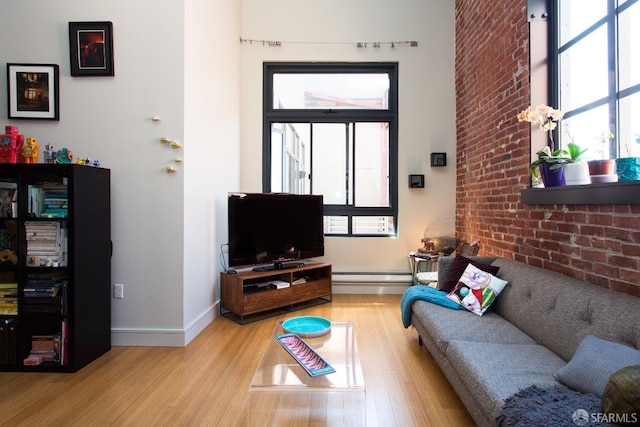 living room with wood finished floors, healthy amount of natural light, a baseboard radiator, brick wall, and baseboards