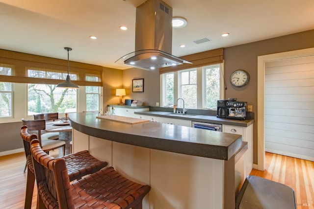 kitchen featuring island exhaust hood, hanging light fixtures, sink, light wood-type flooring, and a breakfast bar area