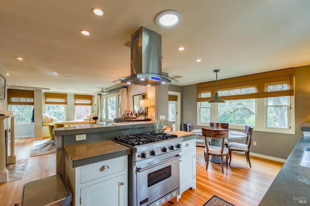 kitchen featuring stainless steel stove, island range hood, white cabinets, light wood-type flooring, and pendant lighting