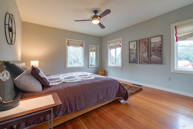 bedroom featuring ceiling fan, wood-type flooring, crown molding, and multiple windows