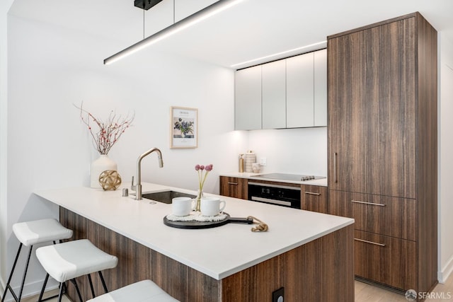 kitchen with a kitchen breakfast bar, white cabinetry, kitchen peninsula, black oven, and sink