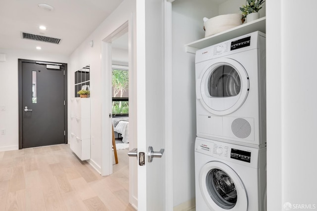 laundry area with light hardwood / wood-style floors and stacked washer and dryer