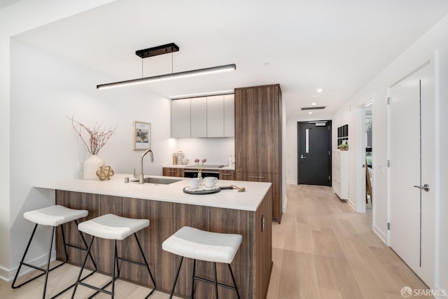 kitchen with a breakfast bar, light hardwood / wood-style floors, sink, white cabinetry, and kitchen peninsula