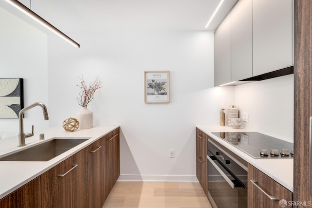 kitchen with black electric stovetop, light hardwood / wood-style floors, sink, white cabinets, and stainless steel oven