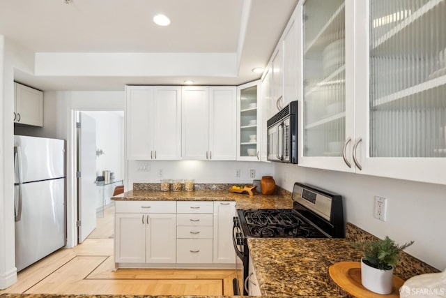 kitchen with white cabinets, glass insert cabinets, stainless steel appliances, and dark stone counters