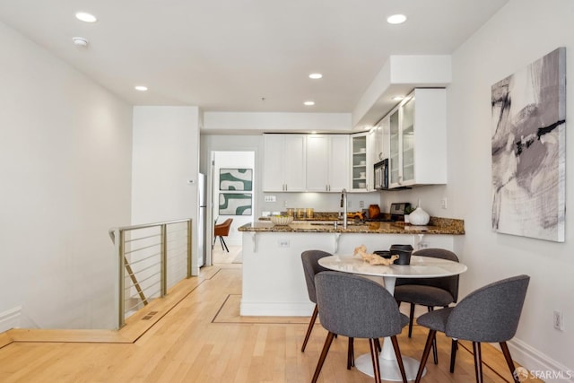 kitchen featuring stainless steel microwave, glass insert cabinets, a sink, dark stone countertops, and light wood-type flooring