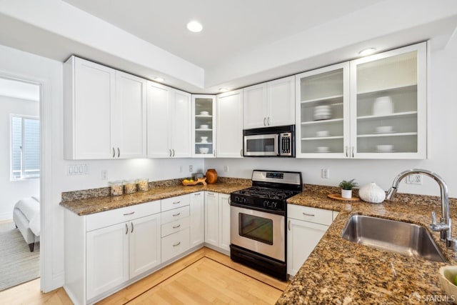 kitchen featuring dark stone countertops, appliances with stainless steel finishes, white cabinets, and a sink