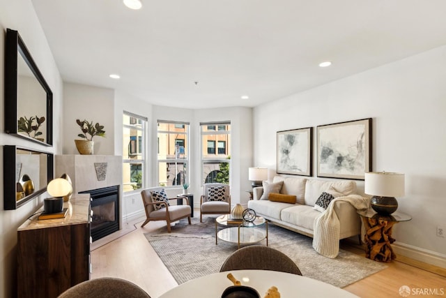 living area with baseboards, light wood finished floors, a glass covered fireplace, and recessed lighting