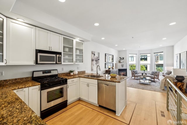 kitchen with a peninsula, appliances with stainless steel finishes, white cabinets, and a sink