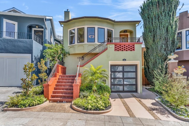 view of front of house featuring driveway, a chimney, stairs, and stucco siding