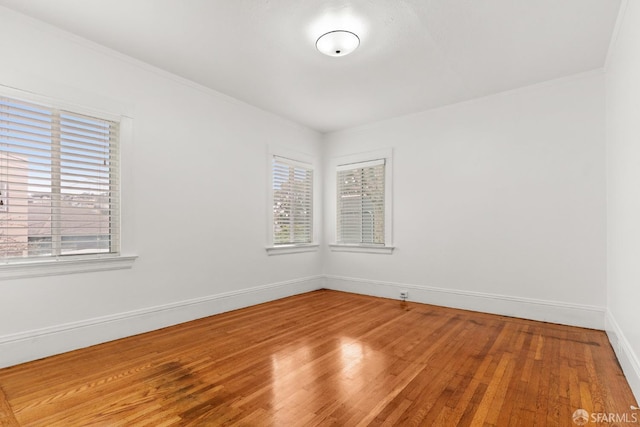 spare room featuring light wood-style floors, crown molding, and baseboards