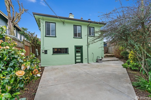 rear view of property with a patio, a chimney, fence, and stucco siding