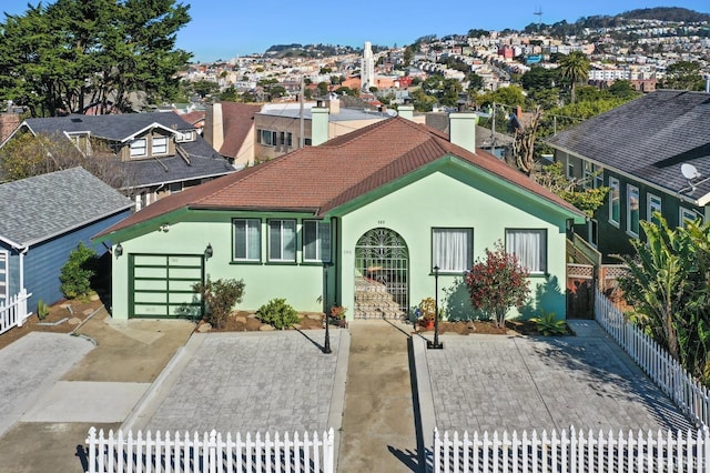 view of front of house with a garage, a tile roof, fence, a residential view, and stucco siding