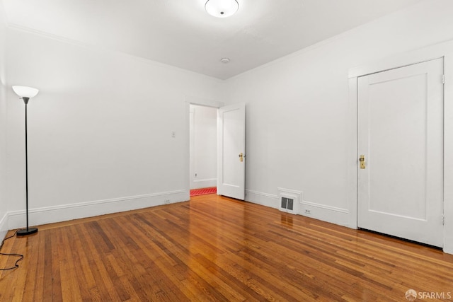 unfurnished bedroom featuring wood-type flooring, crown molding, visible vents, and baseboards