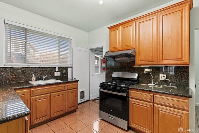 kitchen featuring light tile patterned floors, range with gas stovetop, a sink, under cabinet range hood, and backsplash