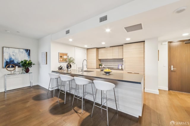 kitchen with dark hardwood / wood-style floors, light brown cabinets, sink, a kitchen bar, and kitchen peninsula