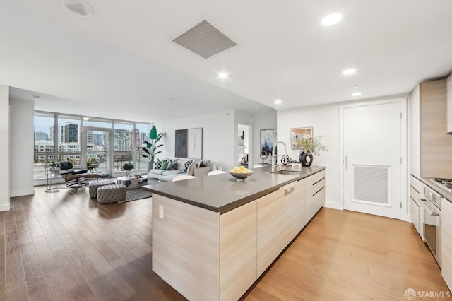 kitchen featuring stainless steel oven, light hardwood / wood-style floors, floor to ceiling windows, light brown cabinets, and sink